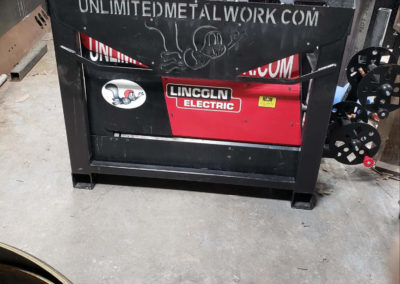 Large red welder inside a steel came with the unlimited metalwork squirrel logo cut in the face